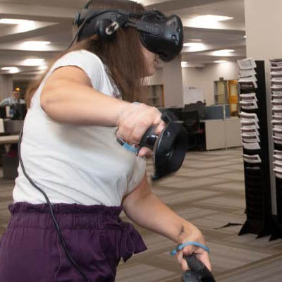 A student wears a VR headset and uses hand controllers.